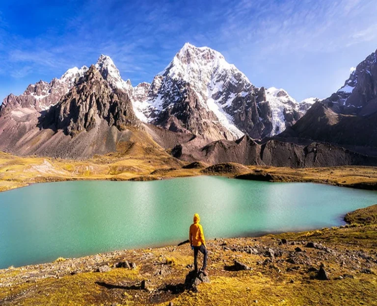 Hiker at one of the seven turquoise lakes of Ausangate surrounded by snow-capped mountains