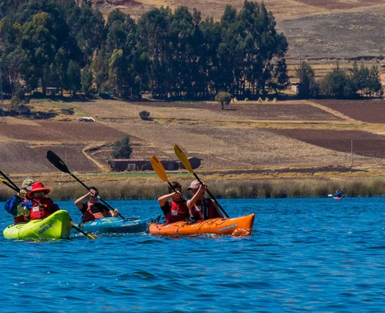 Travelers kayaking on Huaypo Lake in the Sacred Valley with Andean farmland and mountains in the background, Cusco Peru.