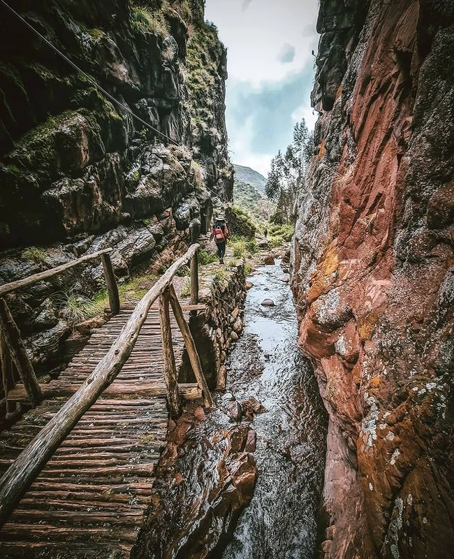 Hiker crossing a wooden bridge along the Huchuy Qosqo trekking route in the Sacred Valley near Cusco, Peru.