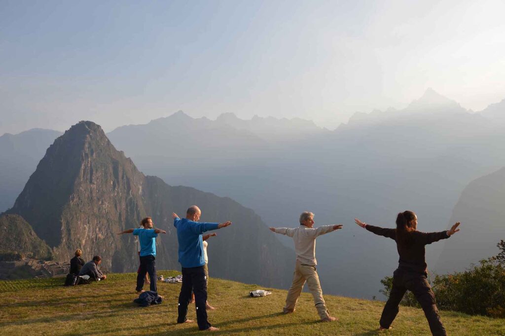 Travelers practicing mindfulness and stretching at sunrise with panoramic views of Machu Picchu and Huayna Picchu mountain