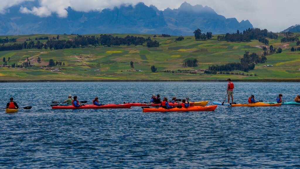 Group of travelers kayaking on a scenic Andean lake surrounded by green fields and mountain landscapes in Peru.