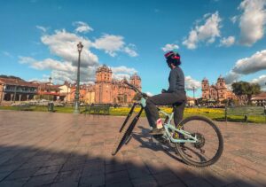 Cyclist riding an bike in Cusco’s Plaza de Armas with the Cathedral and colonial architecture in the background.