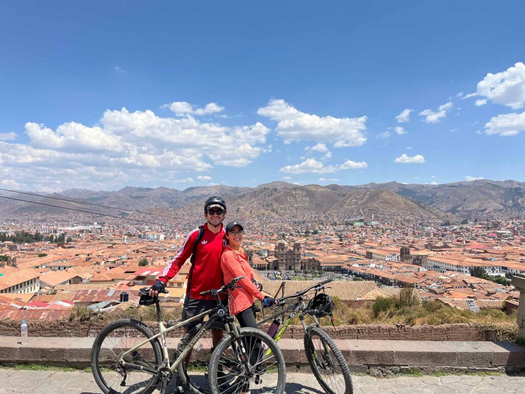 Couple with mountain bikes enjoying a panoramic view of Cusco city and Plaza de Armas from a scenic viewpoint.
