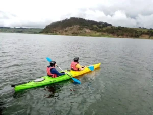 Two travelers kayaking on a high-altitude lake in Cusco, Peru surrounded by hills and cloudy skies.