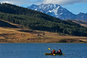 Two travelers kayaking on a lake in the Peruvian Andes with snow-capped mountains in the background.