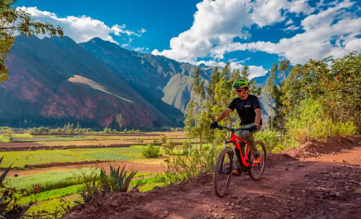 Cyclist riding a mountain bike through the Sacred Valley near Maras and Moray with Andes mountains in the background.