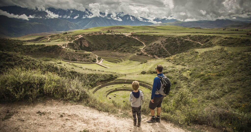 Father and son overlooking the circular Inca terraces of Moray in the Sacred Valley of Cusco, Peru.