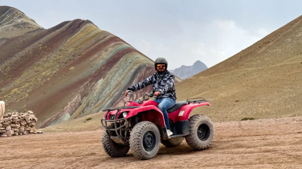 Traveler riding a red ATV near Rainbow Mountain (Vinicunca) surrounded by colorful Andean slopes in Cusco, Peru.
