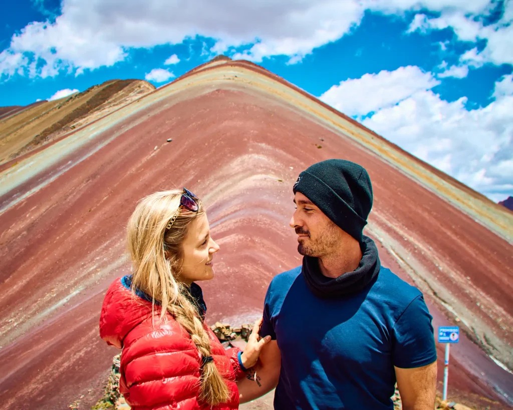 Couple standing in front of Rainbow Mountain (Vinicunca) with colorful red and mineral-striped slopes in Cusco, Peru.