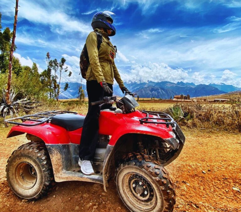 Traveler standing on a red ATV during a Sacred Valley ATV tour in Cusco, Peru with Andean mountains in the background.