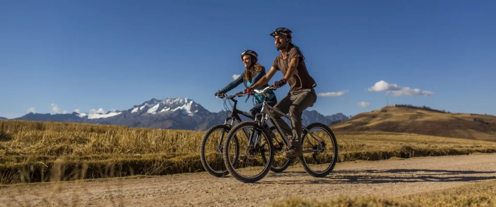 Couple mountain biking in the Sacred Valley near Cusco with snow-capped Andes mountains in the background.