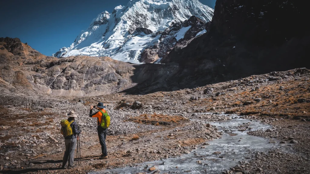 Two hikers standing beside an icy river with the snowy Salkantay mountain in the background during the Salkantay Trek Challenge 3 Days
