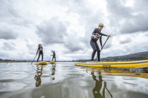 Group of travelers practicing stand up paddle on a lake in the Sacred Valley of Cusco under a dramatic cloudy sky, Peru.