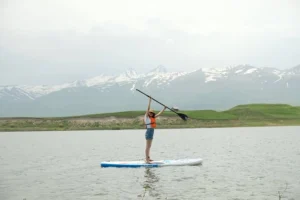Woman enjoying stand up paddle on Huaypo Lake with snow-capped Andes mountains in the background, Sacred Valley Cusco Peru.