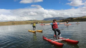 Tourists enjoying a water bike experience on a scenic lake in Peru with mountain views.