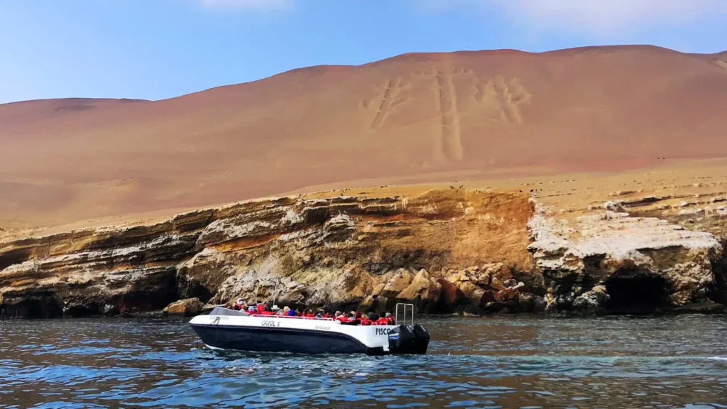 Tourist boat passing the Paracas Candelabro geoglyph on the desert coastline of Peru