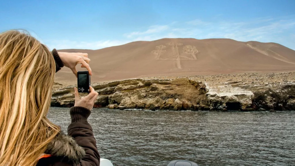 Tourist taking a photo of the Paracas Candelabro geoglyph from a boat along the desert coast of Peru